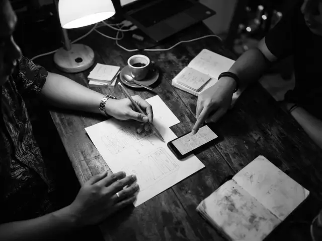 Dua orang membahas sketsa tata letak website di atas meja